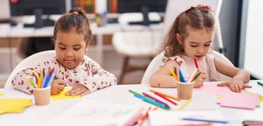 Two kids preschool students sitting on table drawing on paper at classroom