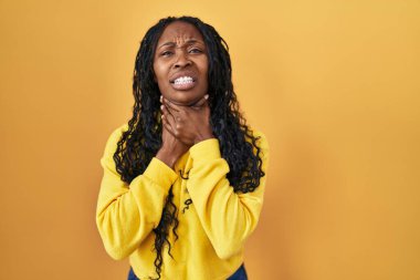 African woman standing over yellow background shouting and suffocate because painful strangle. health problem. asphyxiate and suicide concept. 