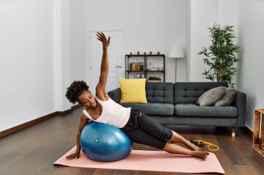 Afrika kökenli Amerikalı kadın evde formda top kullanarak karın kaslarını çalıştırıyor.