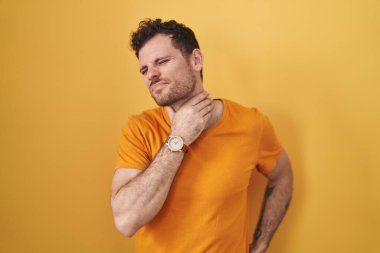 Young hispanic man standing over yellow background touching painful neck, sore throat for flu, clod and infection 