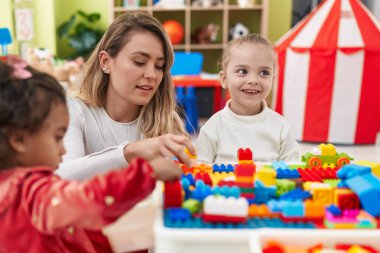 Teacher with girls playing with construction blocks sitting on table at kindergarten