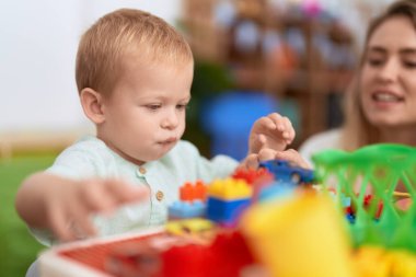 Teacher and toddler playing with construction blocks sitting on table at kindergarten