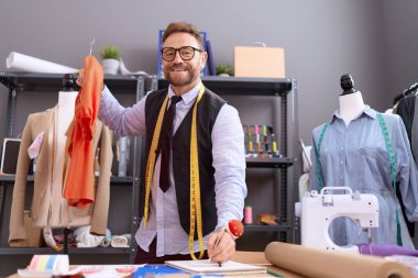 Middle age man tailor holding t shirt writing on notebook at atelier