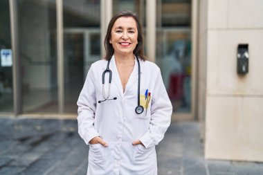 Orta yaşlı kadın doktor üniforması giyiyor. Gülümsüyor.