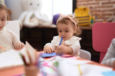 Anaokulundaki masada oturan iki küçük kız deftere resim çiziyor.