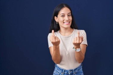 Young hispanic woman standing over blue background showing middle finger doing fuck you bad expression, provocation and rude attitude. screaming excited 