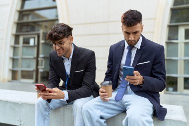 Two hispanic men business workers using smartphones drinking coffee at street