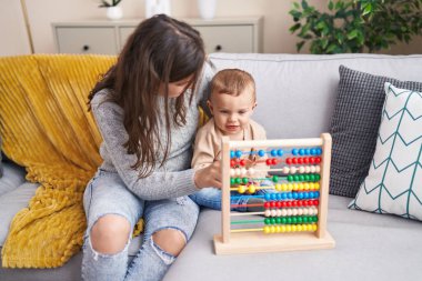 Mother and son playing with abacus sitting on sofa at home
