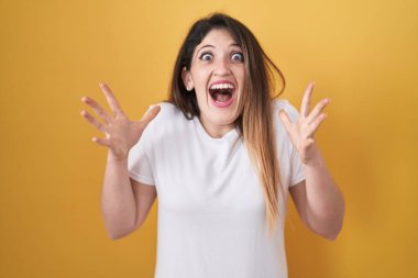 Young brunette woman standing over yellow background celebrating crazy and amazed for success with arms raised and open eyes screaming excited. winner concept 