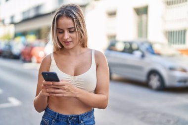 Sokakta akıllı telefon kullanan, kendine güvenen genç sarışın kadın.