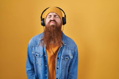 Caucasian man with long beard listening to music using headphones looking at the camera blowing a kiss on air being lovely and sexy. love expression. 