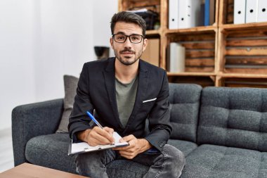 Young hispanic man having psychology session writing on checklist at clinic
