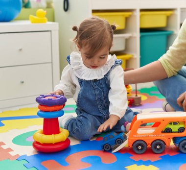 Sevimli sarışın çocuk yerde oturmuş anaokulunda kamyonla oynuyor.