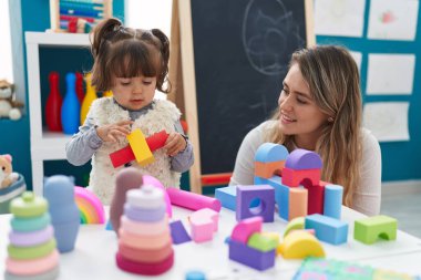 Teacher and toddler playing with toys sitting on table at kindergarten