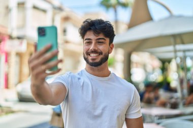 Genç İspanyol adam gülümsüyor. Sokakta akıllı telefonun yanında özçekim yapıyor.