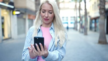 Sokakta akıllı telefon kullanan genç sarışın kadın.