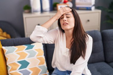 Evdeki kanepede oturan genç ve güzel İspanyol kadın stresli.