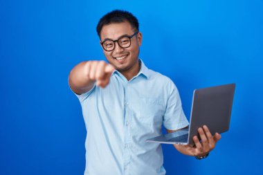 Chinese young man using computer laptop pointing to you and the camera with fingers, smiling positive and cheerful 