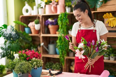 Young beautiful hispanic woman florist holding bouquet of flowers at flower shop