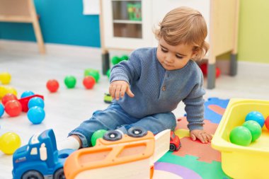 Anaokulunda rahat bir ifadeyle yerde oturan sevimli İspanyol çocuk.