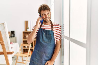 Genç İspanyol adam gülümsüyor. Sanat stüdyosundaki akıllı telefondan konuşuyor.