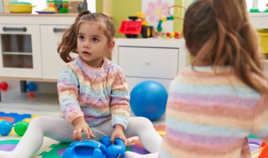 Anaokulunda yerde oturan iki çocuk telefon oyuncağıyla oynuyor.