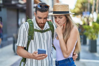 Man and woman tourist couple using smartphone with serious expression at street