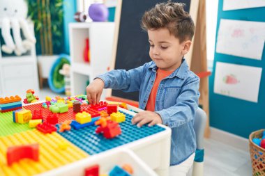 Adorable hispanic toddler playing with construction blocks sitting on table at kindergarten