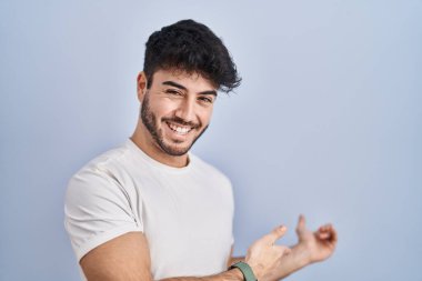 Hispanic man with beard standing over white background inviting to enter smiling natural with open hand 