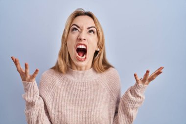 Mavi arka planda dikilen İspanyol kadın deli gibi bağırıyor ve bağırıyor. Saldırgan bir ifade ve kollar havada. hüsran kavramı. 