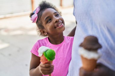 Father and daughter eating ice cream walking together at street