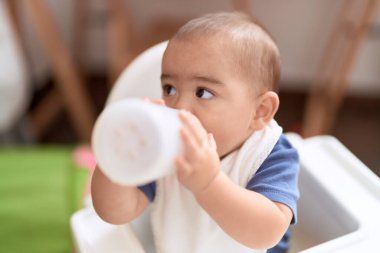 Sevimli Çinli çocuk su içiyor. Evdeki yemek sandalyesinde oturuyor.