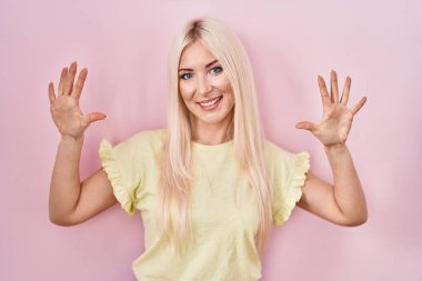 Caucasian woman standing over pink background showing and pointing up with fingers number ten while smiling confident and happy. 