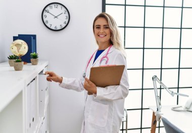 Young woman wearing doctor uniform holding clipboard at clinic