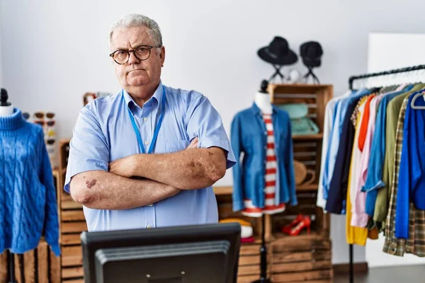 Senior man with grey hair working as manager at retail boutique skeptic and nervous, disapproving expression on face with crossed arms. negative person.