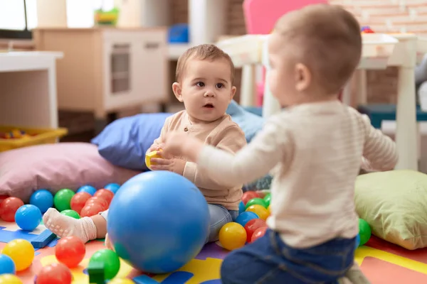 幼稚園の床に座ってボールで遊んでいる2人の愛らしい幼児 — ストック写真