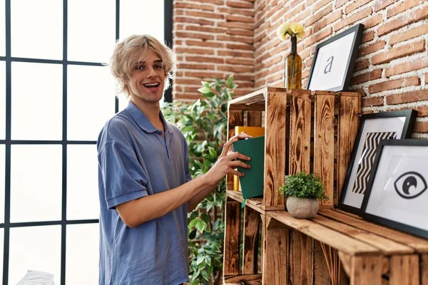 Young blond man holding book standing at home