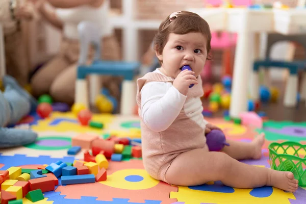 可爱的幼儿咬塑料食物玩具坐在幼稚园的地板上 — 图库照片