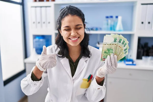 お金を保持している科学研究所で働いている暗い髪を持つヒスパニック女性笑顔と正 親指アップ行う優れたと承認サイン — ストック写真