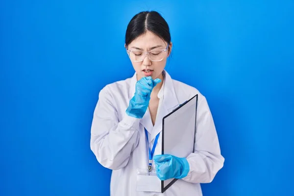 Chinese young woman working at scientist laboratory feeling unwell and coughing as symptom for cold or bronchitis. health care concept.