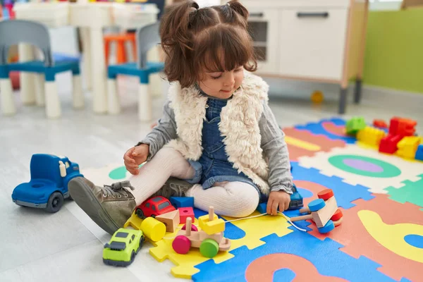 Adorable hispanic toddler playing with car toy sitting on floor at kindergarten