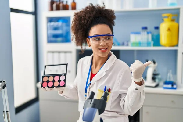 在科学家实验室工作的年轻的非洲裔美国妇女把大拇指指向旁边 高兴地张开嘴笑着 — 图库照片