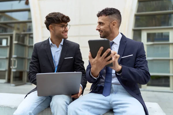 Two hispanic men business workers using touchpad and laptop working at street
