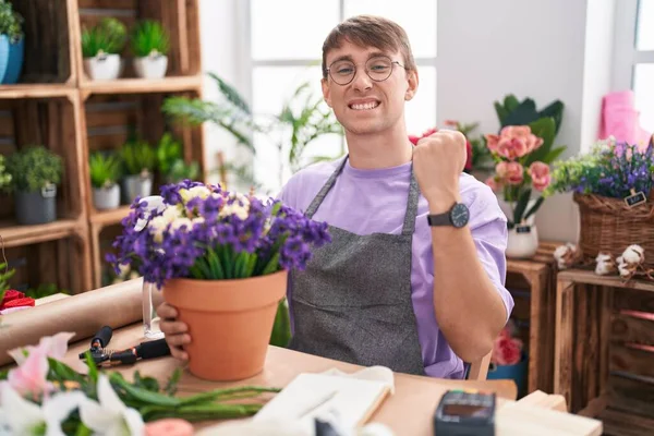 Caucasian blond man working at florist shop very happy and excited doing winner gesture with arms raised, smiling and screaming for success. celebration concept. 