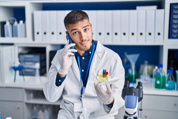 Young hispanic man scientist talking on the smartphone at laboratory
