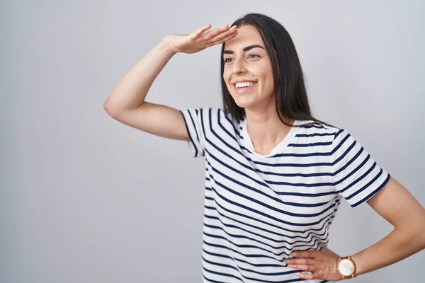 若いブルネットの女性は縞模様のTシャツを着て非常に幸せと笑顔遠くに頭の上に手で見ている 検索の概念 — ストック写真