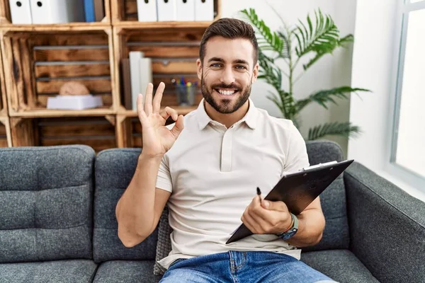 Handsome Hispanic Man Holding Clipboard Working Psychology Clinic Smiling Positive — Stock Photo, Image