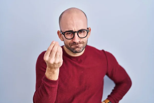 Young bald man with beard standing over white background wearing glasses doing italian gesture with hand and fingers confident expression