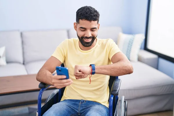 Young Arab Man Using Smartphone Looking Watch Sitting Wheelchair Home — ストック写真