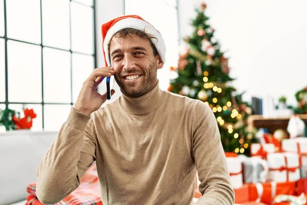 年轻的他惊慌失措的男人坐在家里的圣诞树旁 用智能手机聊天 — 图库照片